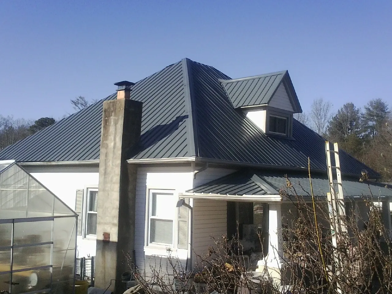 Dark blue standing seam metal roof on a white farmhouse with dormer — Slate & Tile Roof Repair by Roofing Brothers in Thayer