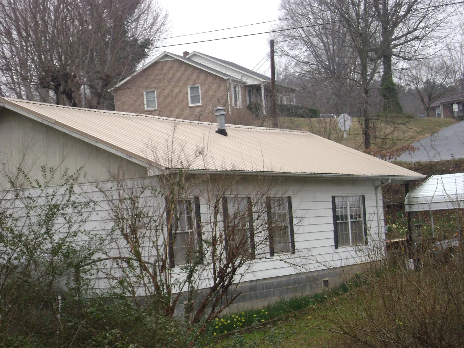 Tan metal roof on a white sided house set into a hillside — Commercial Roofing by Roofing Brothers in Thayer